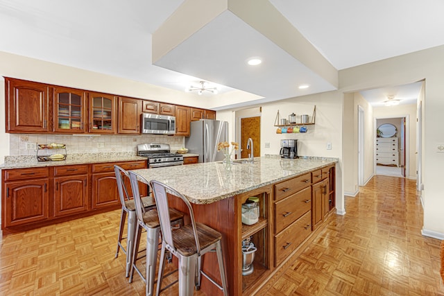 kitchen with appliances with stainless steel finishes, tasteful backsplash, light stone counters, a breakfast bar, and light parquet flooring