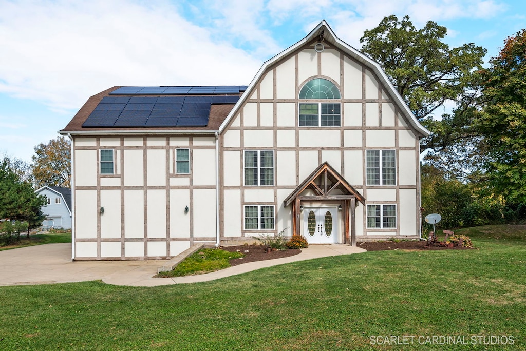 tudor-style house featuring a front yard, solar panels, and french doors