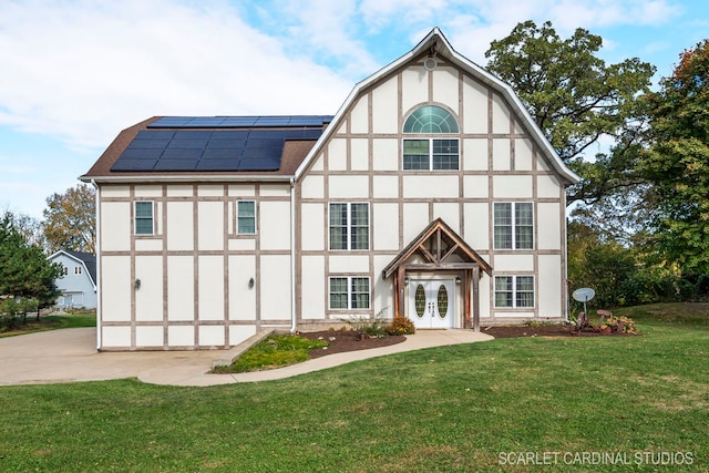 tudor-style house featuring a front yard, solar panels, and french doors