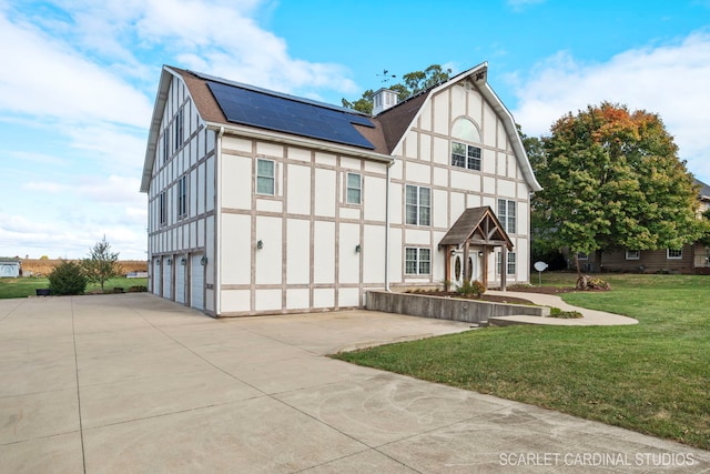 tudor house with a garage, a front yard, and solar panels