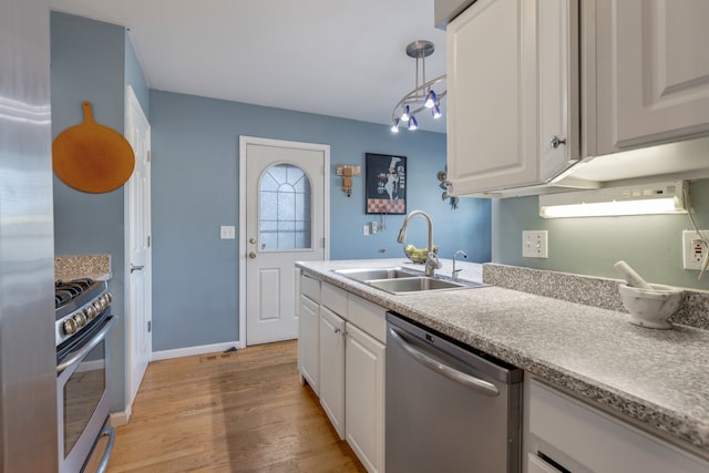 kitchen with sink, hanging light fixtures, white cabinetry, stainless steel appliances, and light hardwood / wood-style flooring