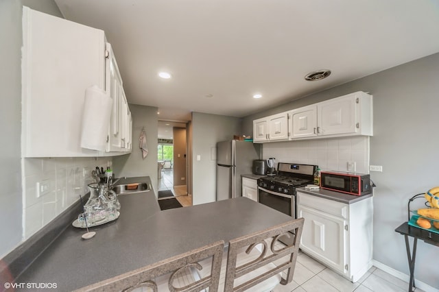 kitchen featuring backsplash, sink, light tile patterned flooring, white cabinetry, and appliances with stainless steel finishes