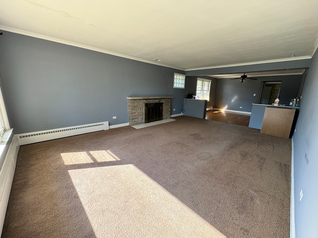 unfurnished living room with ceiling fan, a stone fireplace, a baseboard heating unit, dark colored carpet, and crown molding