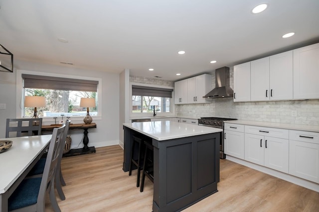 kitchen with wall chimney exhaust hood, a breakfast bar area, stainless steel gas range oven, white cabinetry, and a kitchen island