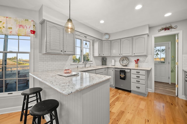 kitchen with stainless steel dishwasher, gray cabinets, hanging light fixtures, and a healthy amount of sunlight