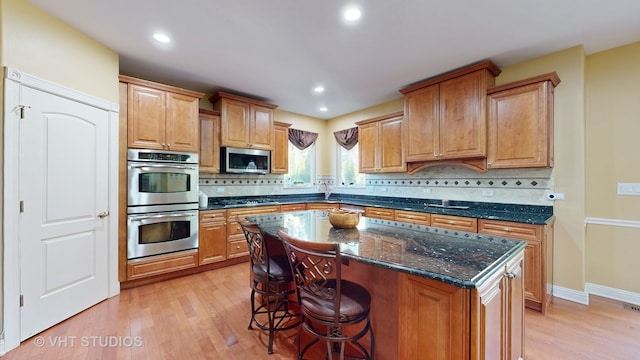 kitchen featuring tasteful backsplash, a center island, light hardwood / wood-style floors, stainless steel appliances, and dark stone counters