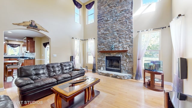 living room featuring a stone fireplace, a towering ceiling, and light wood-type flooring