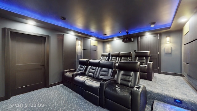 home theater room featuring a tray ceiling and dark carpet