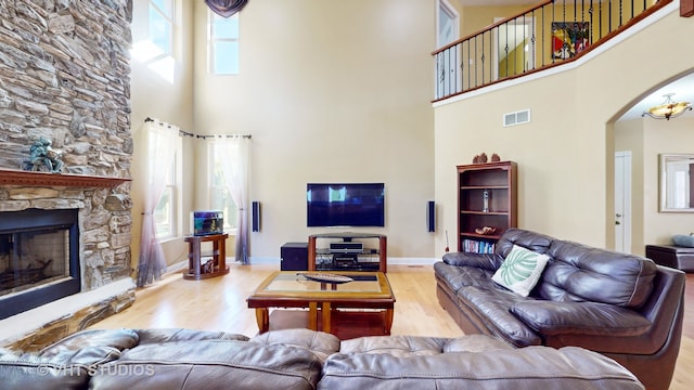 living room featuring a stone fireplace, a high ceiling, and light wood-type flooring