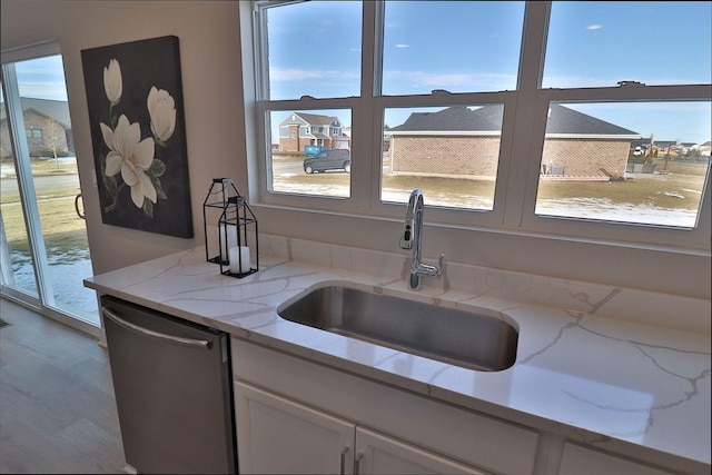 kitchen featuring sink, stainless steel dishwasher, white cabinets, and light stone counters