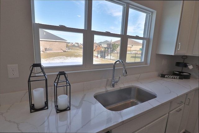 kitchen with white cabinetry, plenty of natural light, sink, and light stone counters