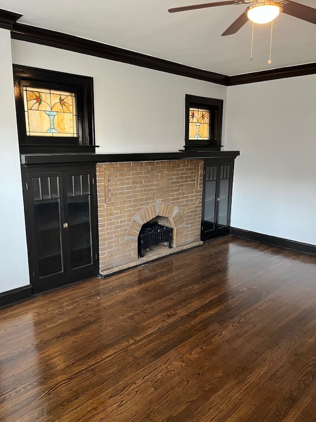 unfurnished living room featuring crown molding, ceiling fan, dark wood-type flooring, and a brick fireplace