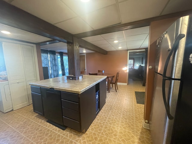 kitchen with tile countertops, stainless steel fridge, a paneled ceiling, and a kitchen island