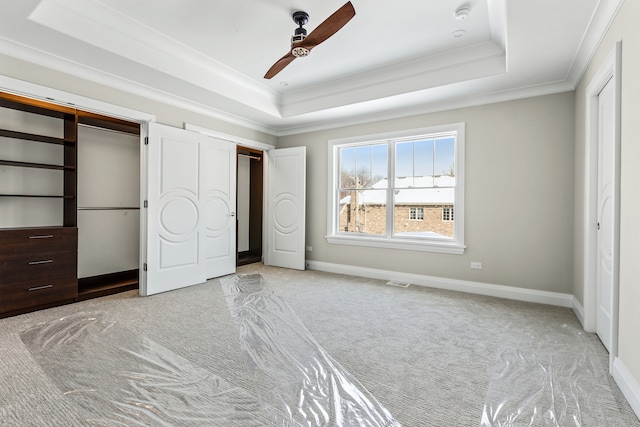 unfurnished bedroom with crown molding, a raised ceiling, light colored carpet, and ceiling fan