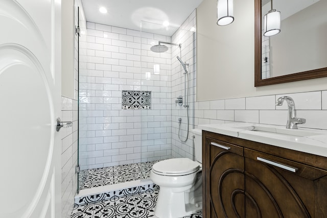 bathroom with a tile shower, tile walls, toilet, vanity, and tile patterned flooring