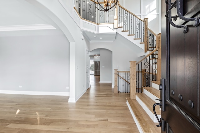 foyer entrance with ornamental molding, light hardwood / wood-style flooring, a high ceiling, and an inviting chandelier