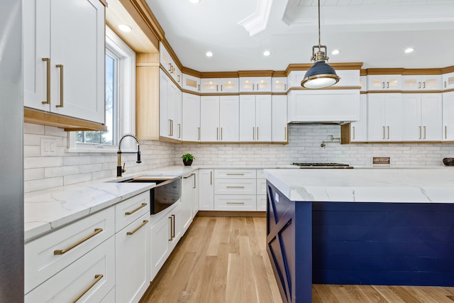 kitchen featuring white cabinets, pendant lighting, light hardwood / wood-style floors, crown molding, and light stone counters