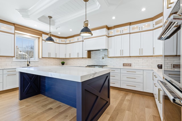 kitchen with hanging light fixtures, backsplash, light stone countertops, light hardwood / wood-style flooring, and crown molding