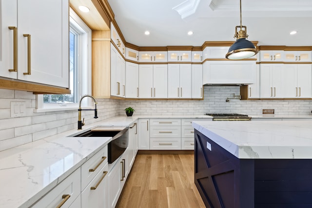 kitchen with tasteful backsplash, hanging light fixtures, white cabinetry, light wood-type flooring, and light stone counters