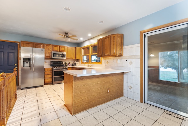 kitchen with kitchen peninsula, stainless steel appliances, light tile patterned flooring, tile walls, and ceiling fan