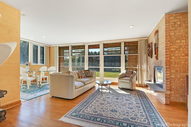 living room featuring a fireplace, a wall of windows, brick wall, and light wood-type flooring