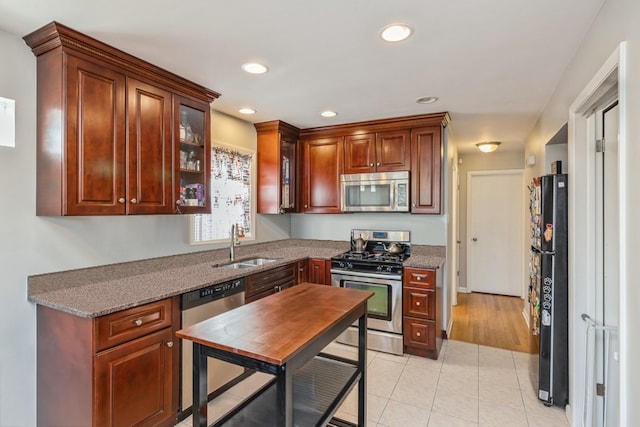 kitchen featuring appliances with stainless steel finishes, dark stone countertops, sink, and light tile patterned floors