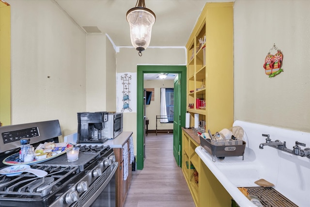 kitchen with stainless steel range with gas cooktop, crown molding, pendant lighting, light wood-type flooring, and a chandelier