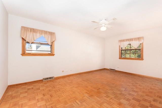 empty room with light parquet floors, a wealth of natural light, and ceiling fan