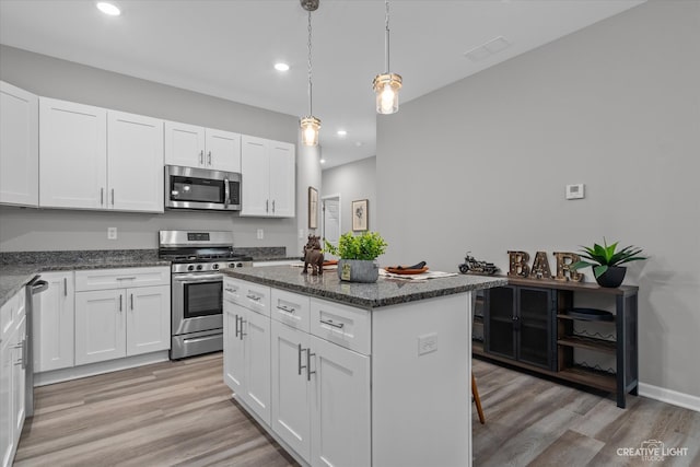 kitchen featuring appliances with stainless steel finishes, a center island, hanging light fixtures, white cabinets, and light hardwood / wood-style flooring