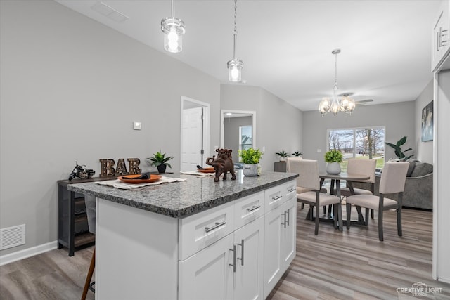 kitchen with a breakfast bar area, a kitchen island, white cabinets, and light hardwood / wood-style flooring