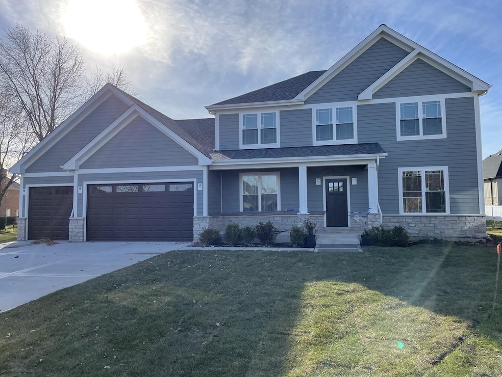 craftsman-style home featuring an attached garage, a shingled roof, a front lawn, concrete driveway, and stone siding