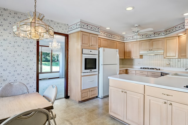 kitchen featuring decorative backsplash, white appliances, pendant lighting, light brown cabinetry, and ceiling fan with notable chandelier