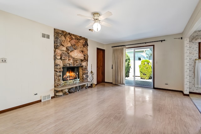 unfurnished living room featuring a stone fireplace, light wood-type flooring, and ceiling fan