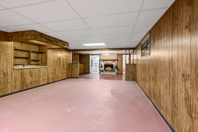 basement featuring a drop ceiling, a fireplace, and wood walls