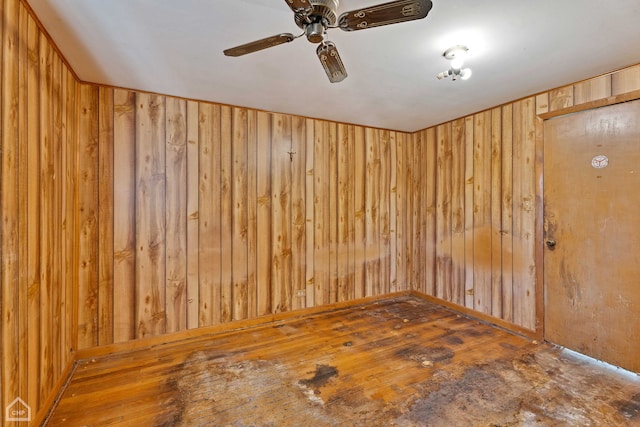 spare room with wooden walls, wood-type flooring, and ceiling fan