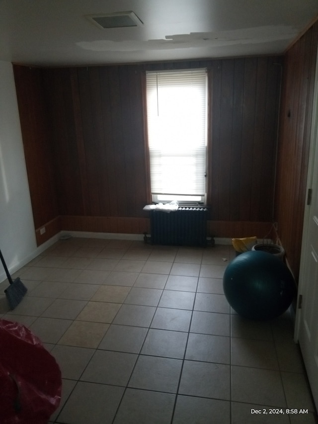 empty room featuring radiator, wooden walls, and light tile patterned floors