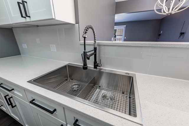 details with light stone counters, sink, an inviting chandelier, and white cabinets