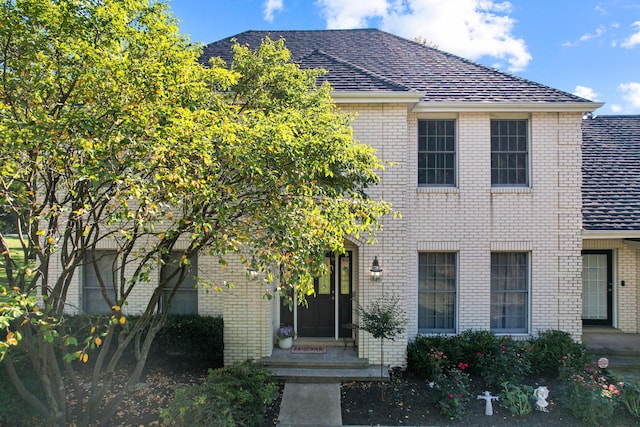 view of front facade with brick siding and roof with shingles