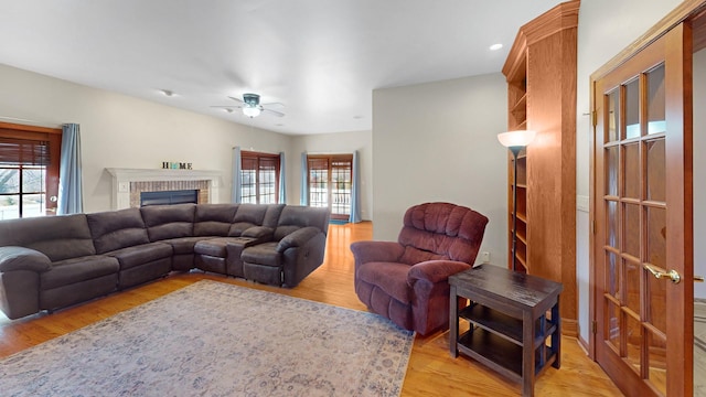 living room featuring light wood-type flooring, a ceiling fan, and a fireplace