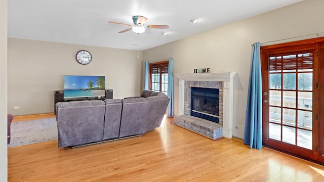 living area featuring a brick fireplace, a ceiling fan, and light wood-style floors