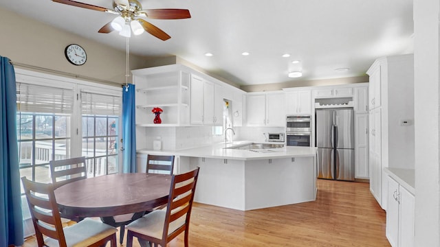 kitchen featuring light wood finished floors, light countertops, a peninsula, white cabinets, and stainless steel appliances