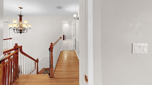 hall with an upstairs landing, a notable chandelier, and wood finished floors