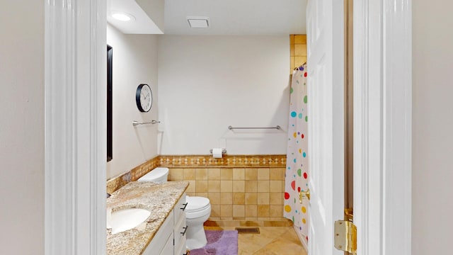 bathroom with toilet, vanity, wainscoting, tile patterned floors, and tile walls