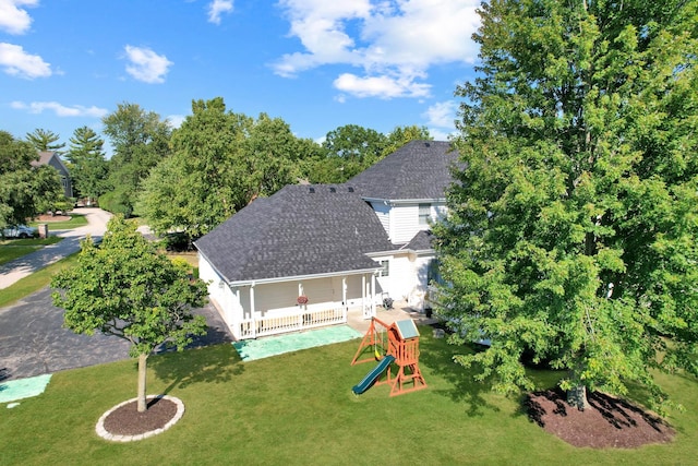 rear view of property featuring a lawn, a shingled roof, and a playground