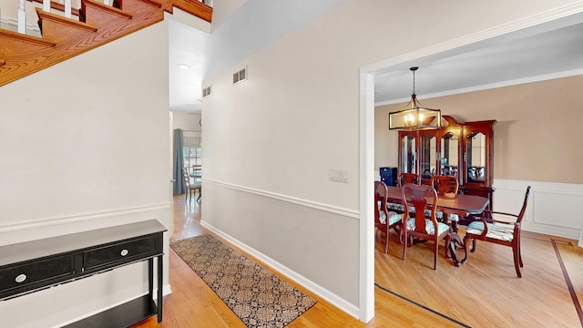 hall featuring crown molding, light wood-style flooring, visible vents, and wainscoting