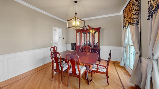 dining area featuring ornamental molding, a notable chandelier, light wood finished floors, and wainscoting