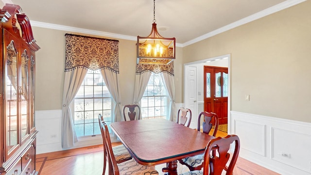 dining space with a chandelier, wainscoting, crown molding, and light wood-style flooring