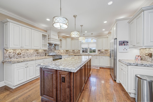 kitchen featuring appliances with stainless steel finishes, custom range hood, decorative light fixtures, light hardwood / wood-style floors, and white cabinetry