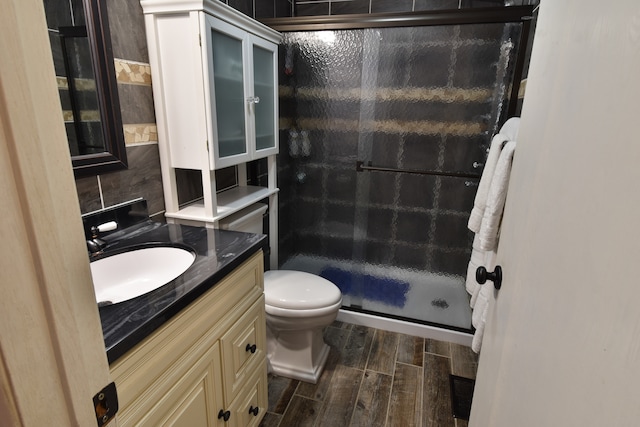 bathroom featuring toilet, hardwood / wood-style floors, vanity, an enclosed shower, and tasteful backsplash