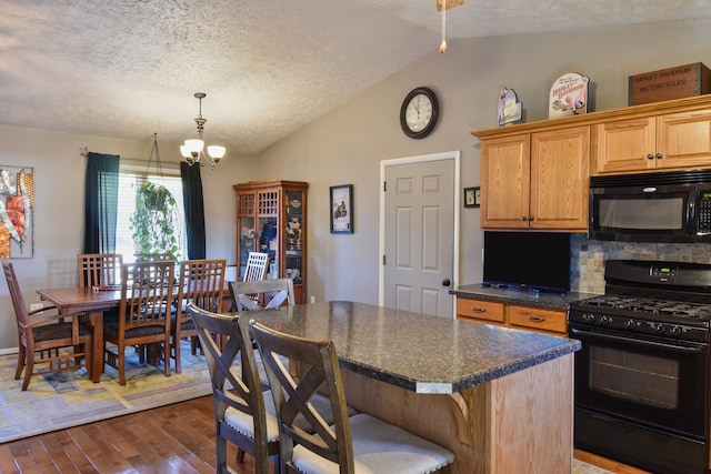 kitchen with vaulted ceiling, dark hardwood / wood-style floors, black appliances, a notable chandelier, and a center island